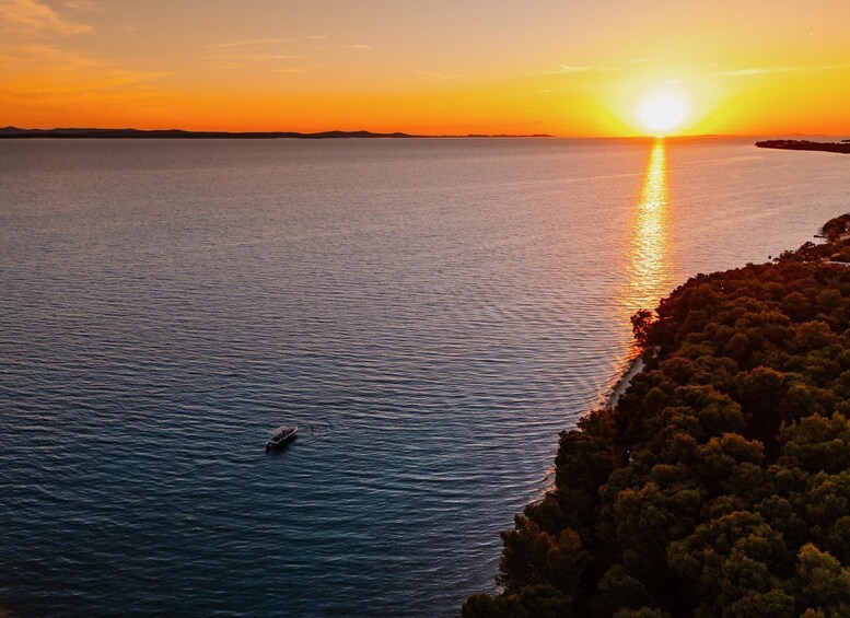 A sunset over a calm sea with a boat and a forested coastline. 5