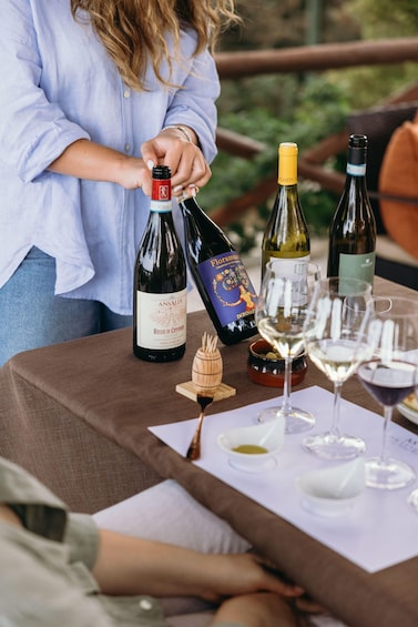 A person pouring wine from a bottle onto a table with several glasses and a wooden bowl. 3