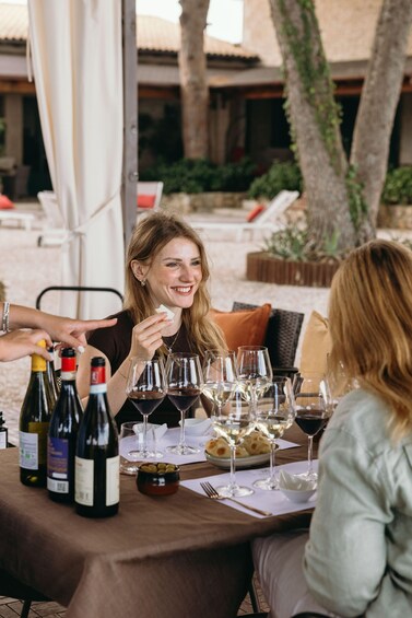 A group of people seated at an outdoor table with wine bottles and glasses, suggesting a social gathering or meal. 1