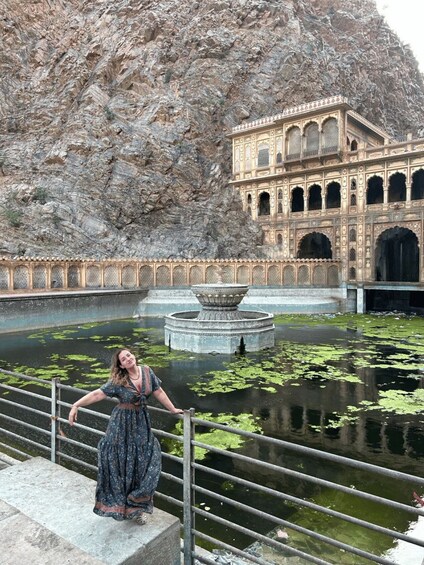 A person standing by a water body with a rocky background and a building with arches. 4