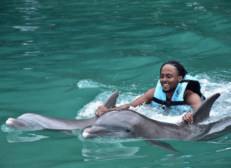 A person in a blue life jacket interacting with a dolphin in clear water. 3