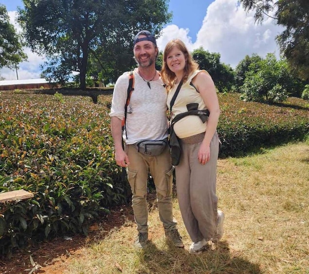 Two people standing in a garden with greenery and trees in the background. 1