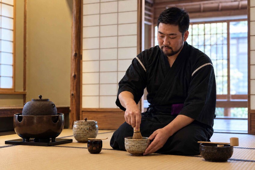 A person sitting on tatami mats, whisking a mixture in a bowl. 2