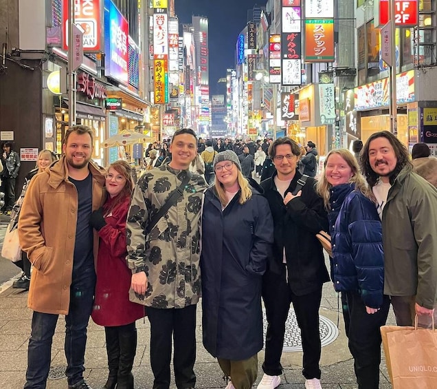 A group of people standing on a busy street at night with illuminated signs and billboards in the background. 5
