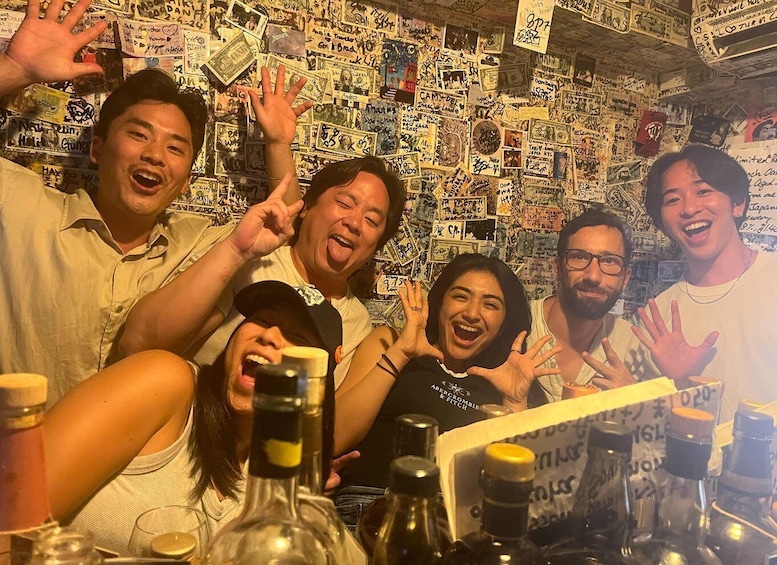 A group of people at a bar with a wall covered in various stickers and notes. 1