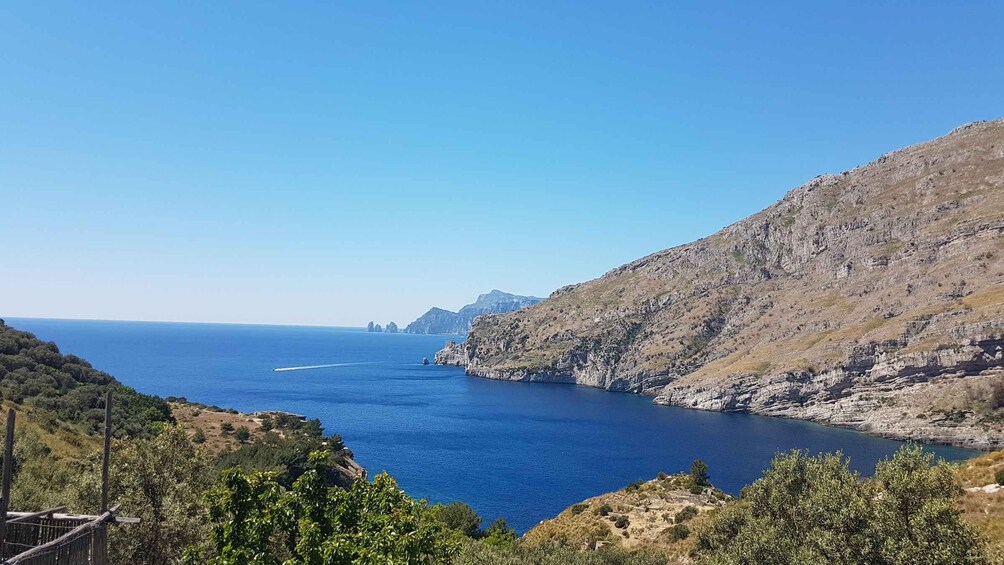 A coastal landscape with a clear blue sea, rocky cliffs, and a boat in the distance. 1