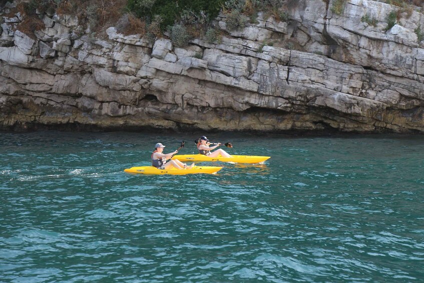 Two people kayaking on a calm body of water with rocky cliffs in the background. 2