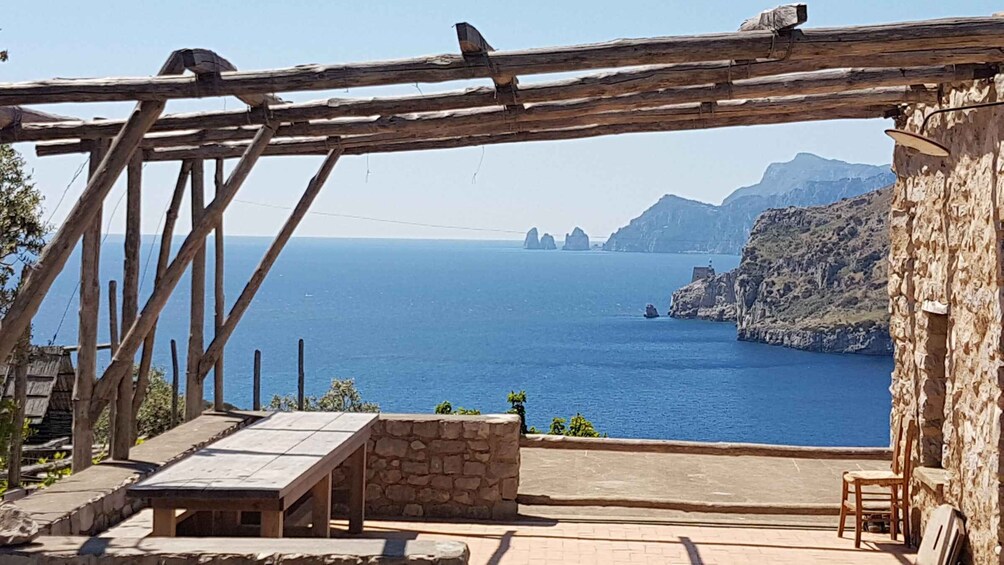 A wooden pergola overlooking a coastal view with a stone bench and a chair. 3