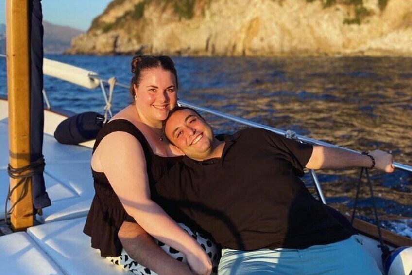 A couple on a sailboat with a rocky coastline in the background. 4