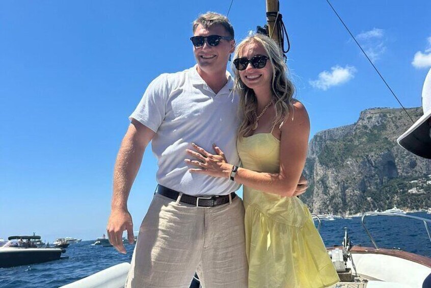 A couple on a sailboat with a mountainous coastline in the background. 5