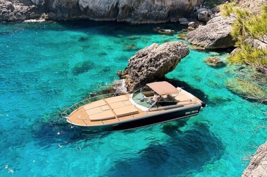 A boat anchored near a rocky shoreline in clear turquoise water. 2