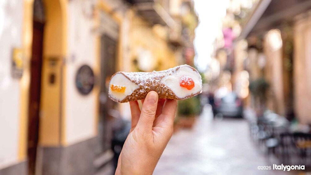A hand holding a cannoli with a creamy filling and a chocolate ball. 3