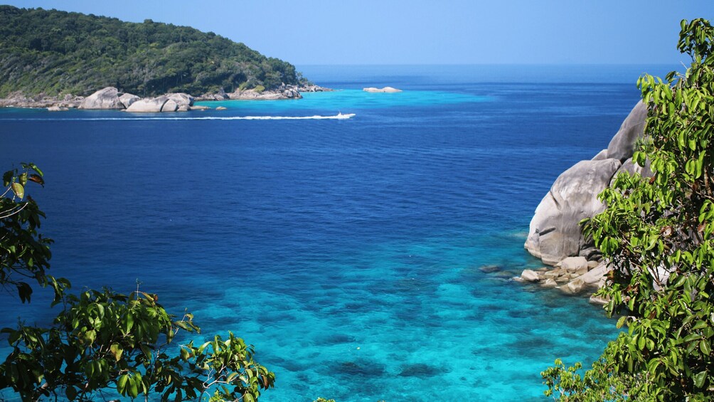 A coastal landscape with clear blue waters, rocky outcrops, and lush greenery. 2