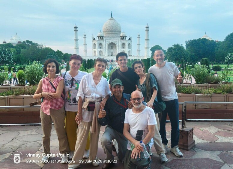 A group of people posing in front of the Taj Mahal with a park and greenery in the background. 5