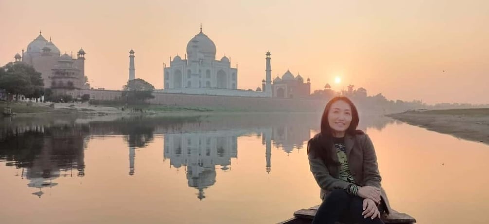 A person sitting by a calm river with the Taj Mahal in the background. 1