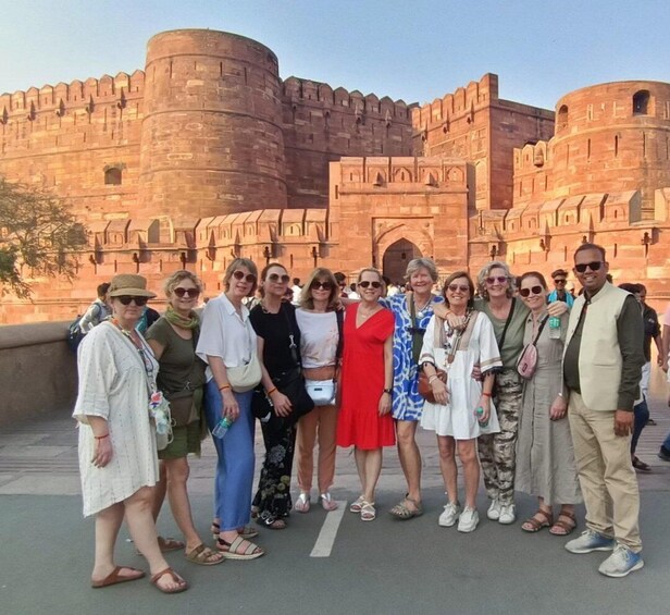 A group of people standing in front of a large, historic fort with crenellated walls and a central tower. 4