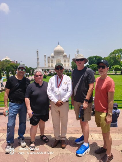 A group of people standing in front of the Taj Mahal with a clear sky in the background. 3