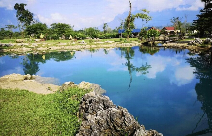 A calm lake with clear reflections, surrounded by greenery and a few buildings in the distance. 5