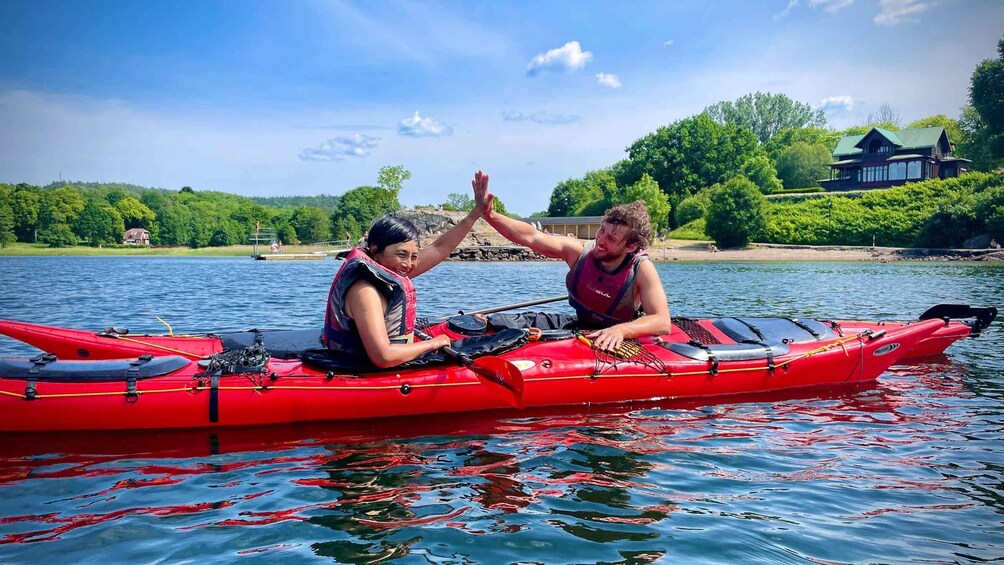 Two people in a red kayak on a calm lake with a house and trees in the background. 5