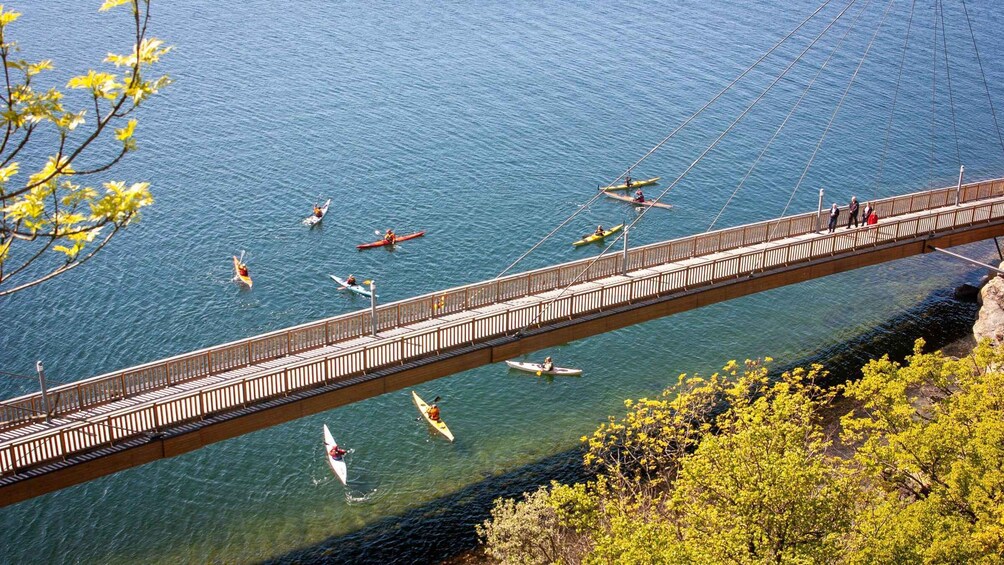 A wooden bridge over a calm lake with kayakers on the water. 1