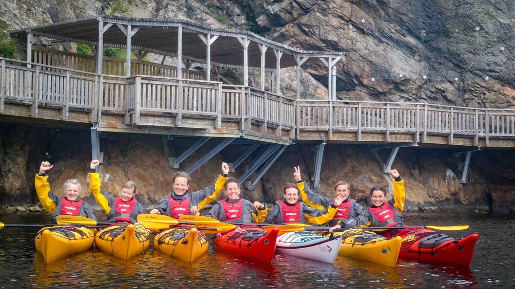 A group of people in kayaks on a river with a wooden bridge in the background. 3