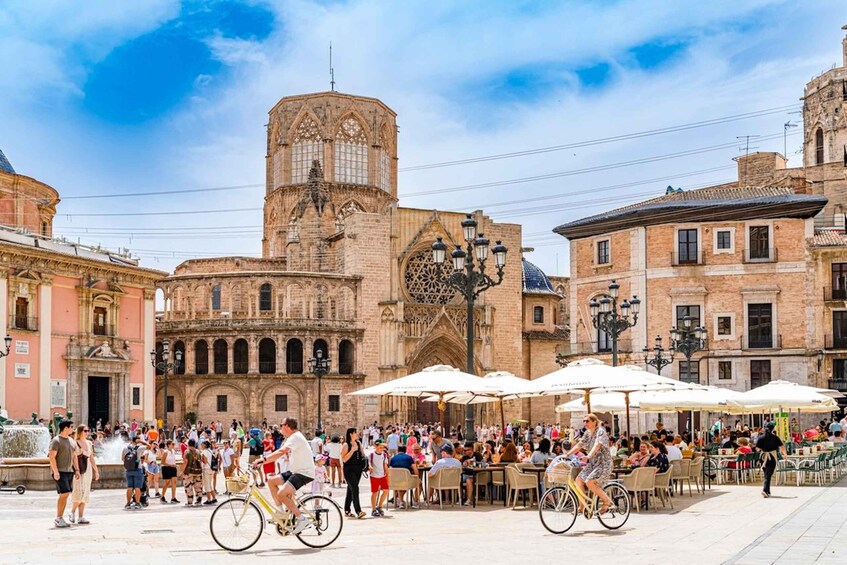 A bustling square with historic architecture, including a prominent tower and a fountain. 3