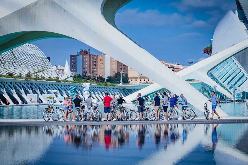 A modern architectural structure with a reflective pool and people standing around bicycles. 4