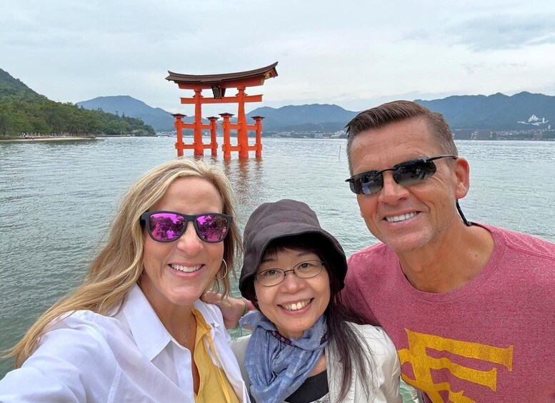 Three people taking a selfie with a traditional Japanese torii gate in the background. 1