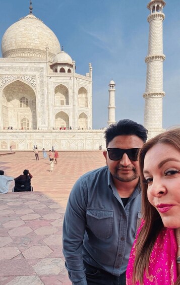 A person in a blue shirt and a woman in a pink dress standing in front of the Taj Mahal. 5