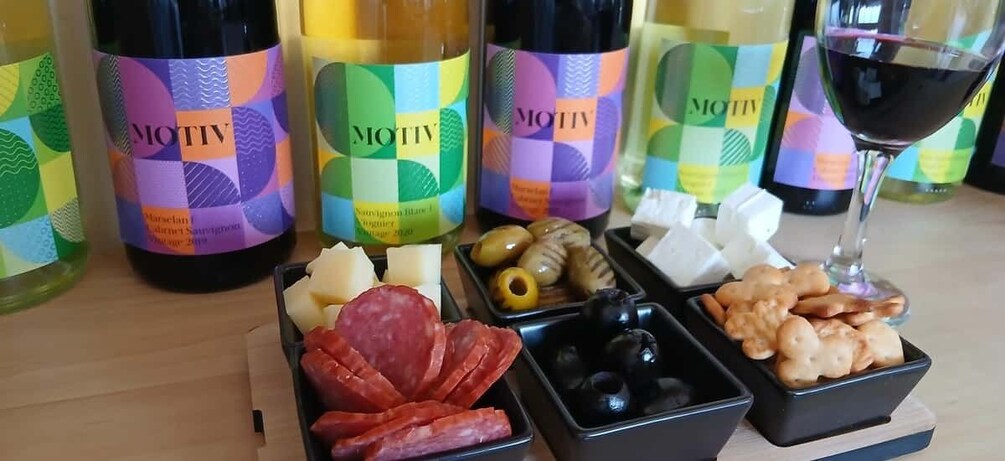 Bottles of MOTIV wine, cheese, olives, and crackers on a table. 1