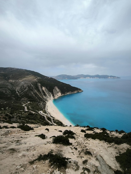 A coastal landscape with a winding road, a sandy beach, and a clear blue sea. 2