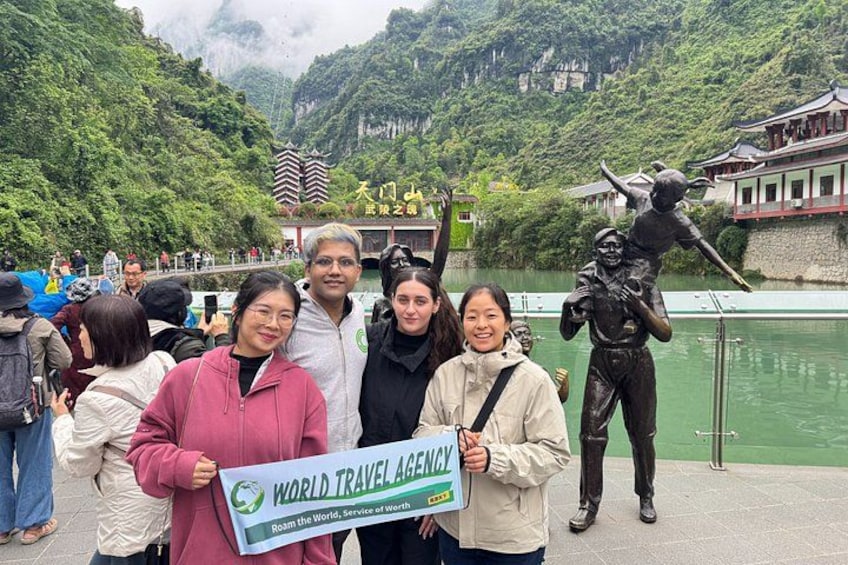 A group of people standing in front of a statue with a sign that reads 'WORLD TRAVEL AGENCY.' 5
