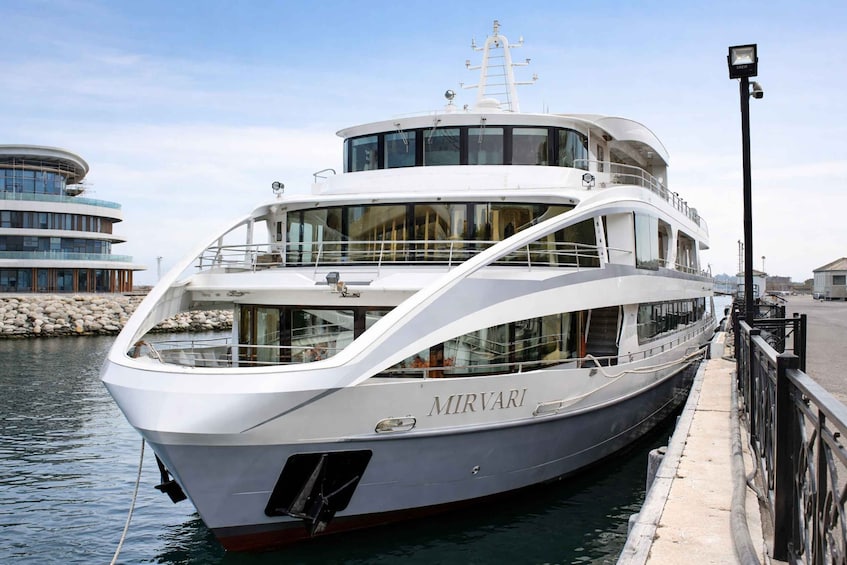 A large, multi-deck yacht named MIRVANI docked at a marina with a modern building in the background. 4