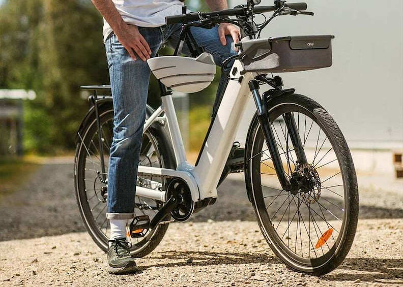 A person standing next to a white electric bicycle with a basket and a kickstand. 3