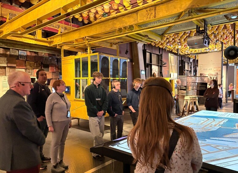 A museum interior with yellow structural elements, a large interactive display, and visitors observing exhibits. 2