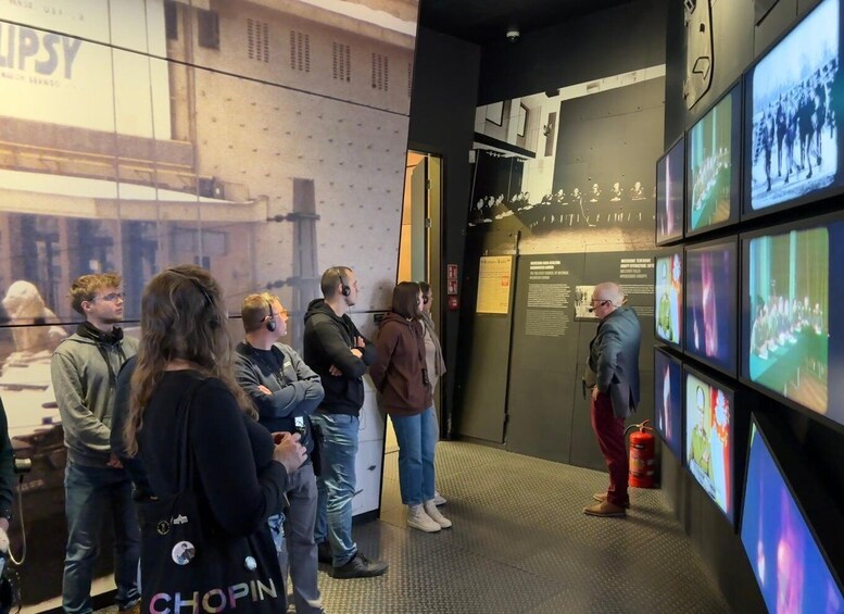 A group of people observing a wall with multiple screens displaying historical footage. 3