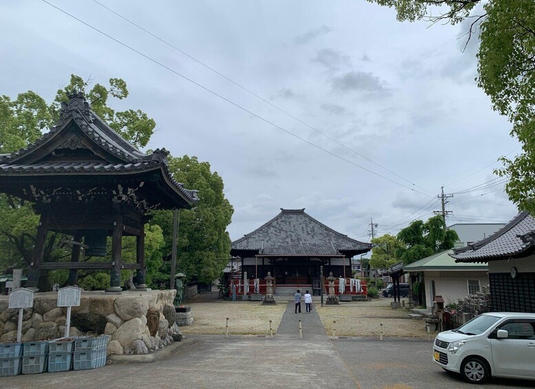 A traditional Japanese temple with a large gate and a smaller pavilion. There are stone lanterns and a stone wall in the foreground. 5