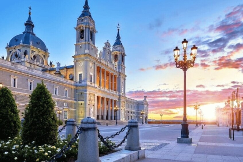 A grand historical building with domes and towers, a well-maintained plaza with a street lamp, and a sunset sky. 3