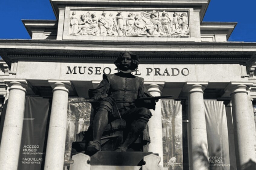 A statue in front of Museo del Prado with columns and a clear blue sky. 4