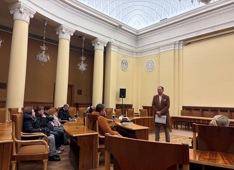 A formal meeting in a room with wooden furniture, white columns, and a glass ceiling. 3