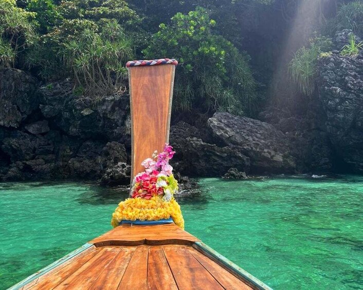A wooden boat with a floral arrangement on the bow, surrounded by clear turquoise water and rocky cliffs. 2