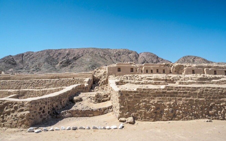 Ancient ruins with stepped structures and a mountainous backdrop. 5