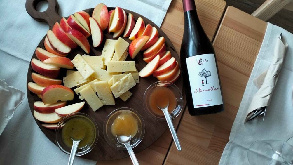A charcuterie board with sliced apples, cheese, and two types of spreads, accompanied by a bottle of rosé wine. 5