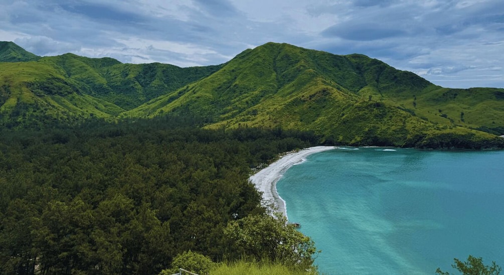 A coastal landscape with a beach, turquoise waters, and green hills. 2