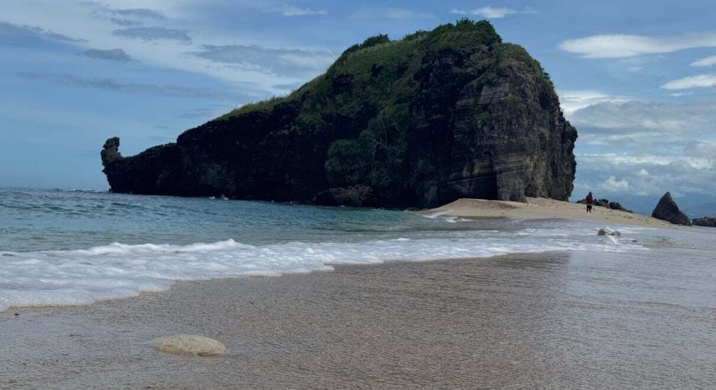 A beach with a large rock formation and waves crashing onto the shore. 4