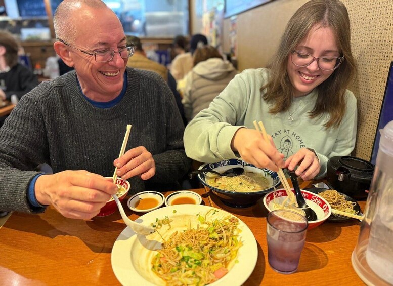 Two people dining at a restaurant with bowls of noodles and chopsticks. 4