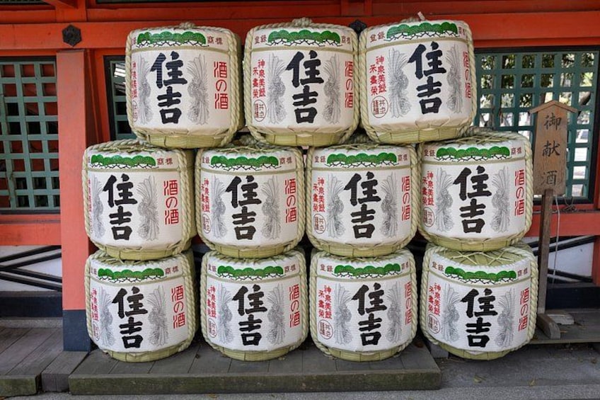 Een stapel grote witte vaten met Japanse tekens, buiten geplaatst tegen een gebouw met een rode gevel en groene raamkozijnen. 4