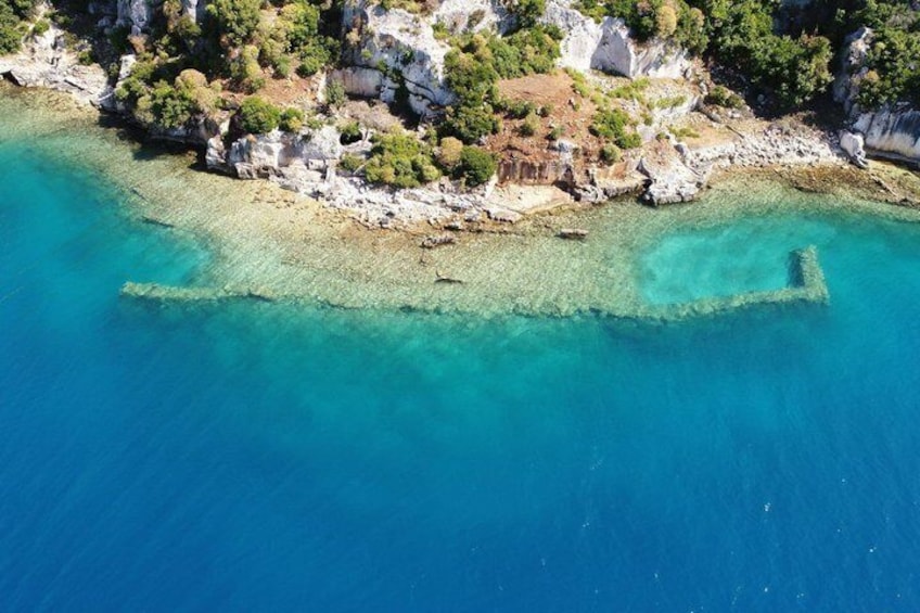 Luchtbeeld van een kustgebied met helder turquoise water, rotsachtige kliffen en schaarse begroeiing. 3