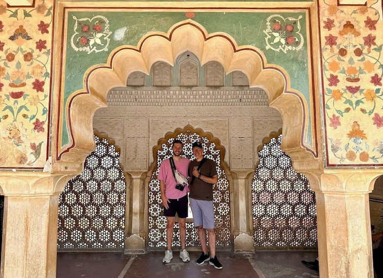 Two people standing in front of a decorative archway with intricate patterns and floral designs. 1