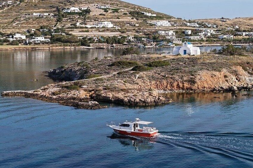 A boat on calm water, a shoreline with white buildings, and a hilly landscape in the background. 1